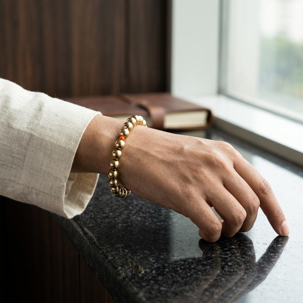 Hand wearing a golden hematite bracelet on a reflective surface with a blurred background